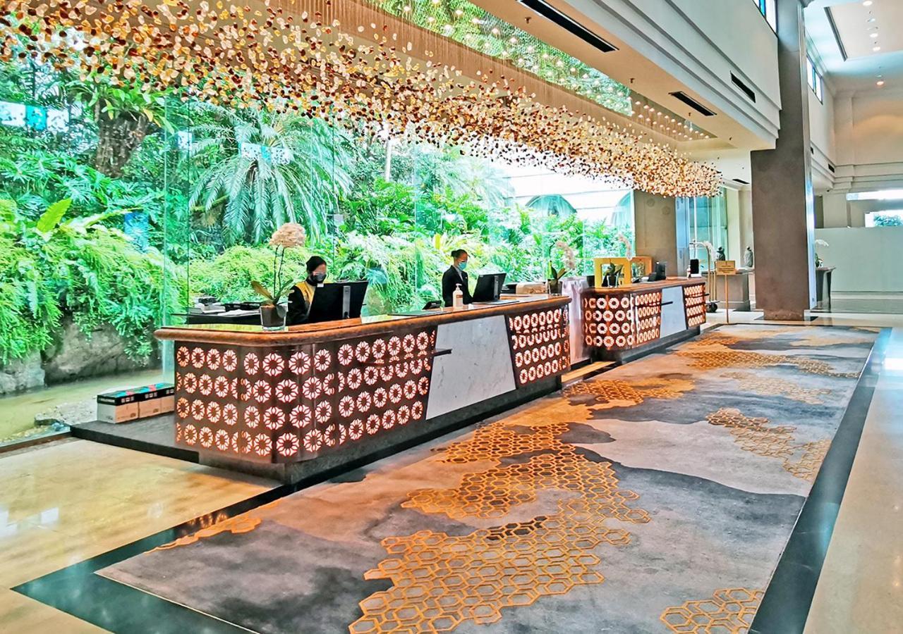 萨马萨玛克利亚酒店 雪邦 外观 照片 The image shows a luxurious hotel lobby with a modern design. In the foreground, there is a stylish reception desk made of wood and decorated with circular patterns. Behind the desk, two staff members are attending to guests. The lobby features a lar