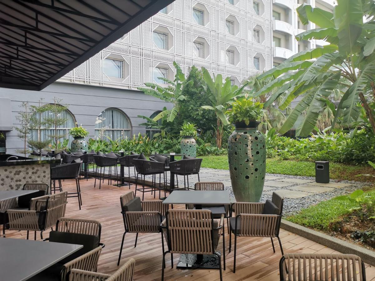 萨马萨玛克利亚酒店 雪邦 外观 照片 The photo depicts an outdoor dining area with several tables and chairs positioned on a wooden patio. In the background, there is a lush garden filled with tropical plants and large green pots containing foliage. The setting appears to be part of a r