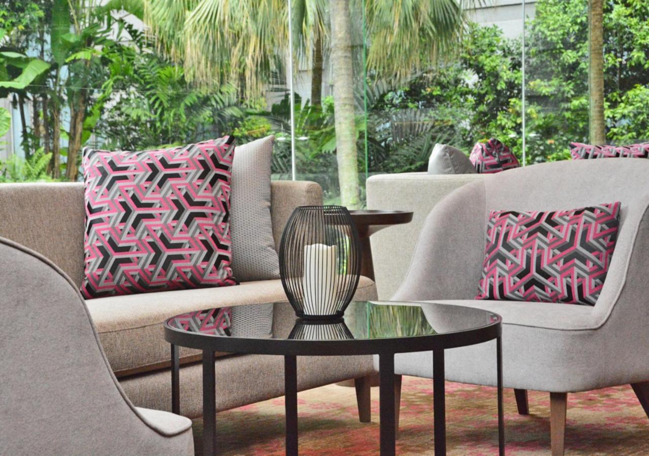 萨马萨玛克利亚酒店 雪邦 外观 照片 The photo shows a cozy seating area that features two modern armchairs upholstered in light gray fabric. Each chair has a decorative cushion with a geometric pattern in shades of pink and black. In the center, there is a small round table with a dark