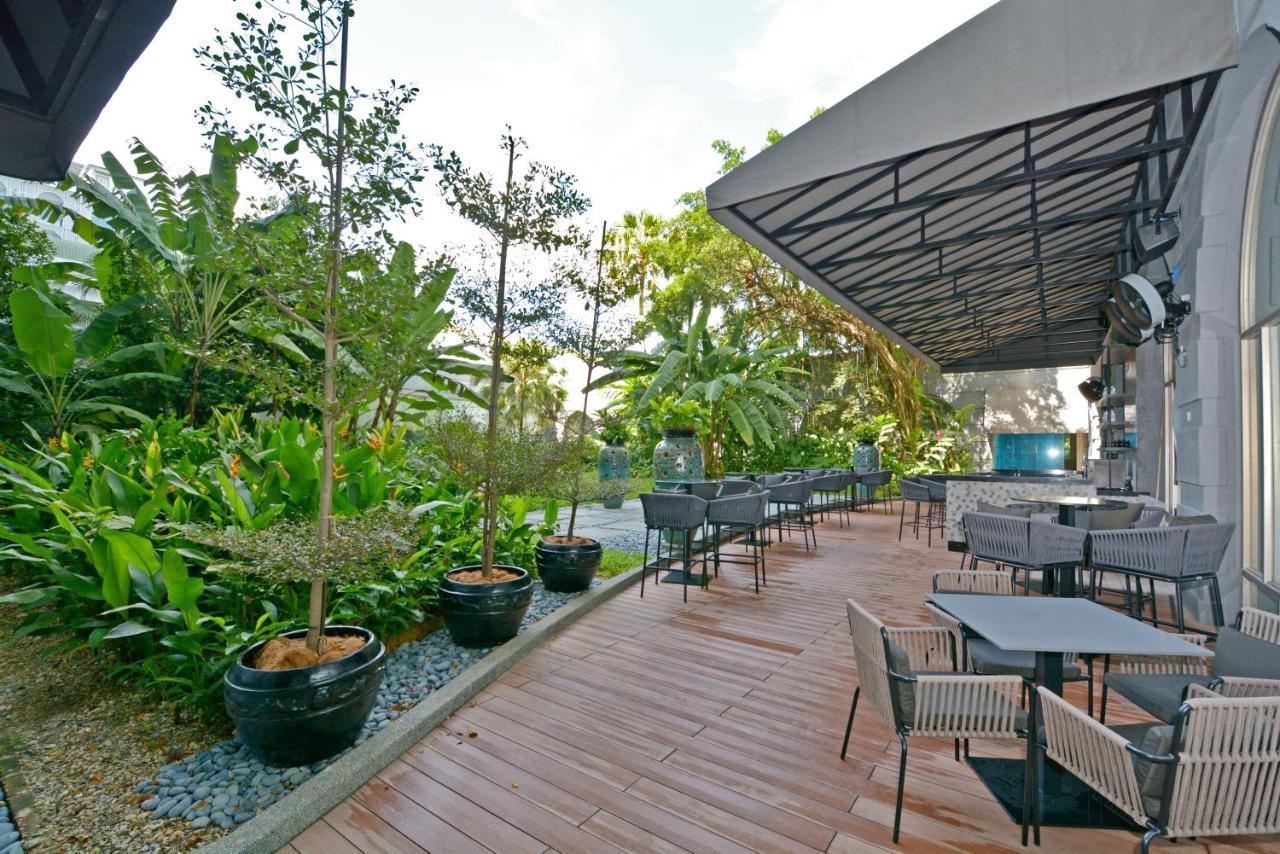 萨马萨玛克利亚酒店 雪邦 外观 照片 The photo shows an outdoor patio area with a wooden deck. There are several tables and chairs arranged neatly under a shaded roof. Surrounding the area are various plants and trees, creating a lush, green environment. The overall setting appears to b