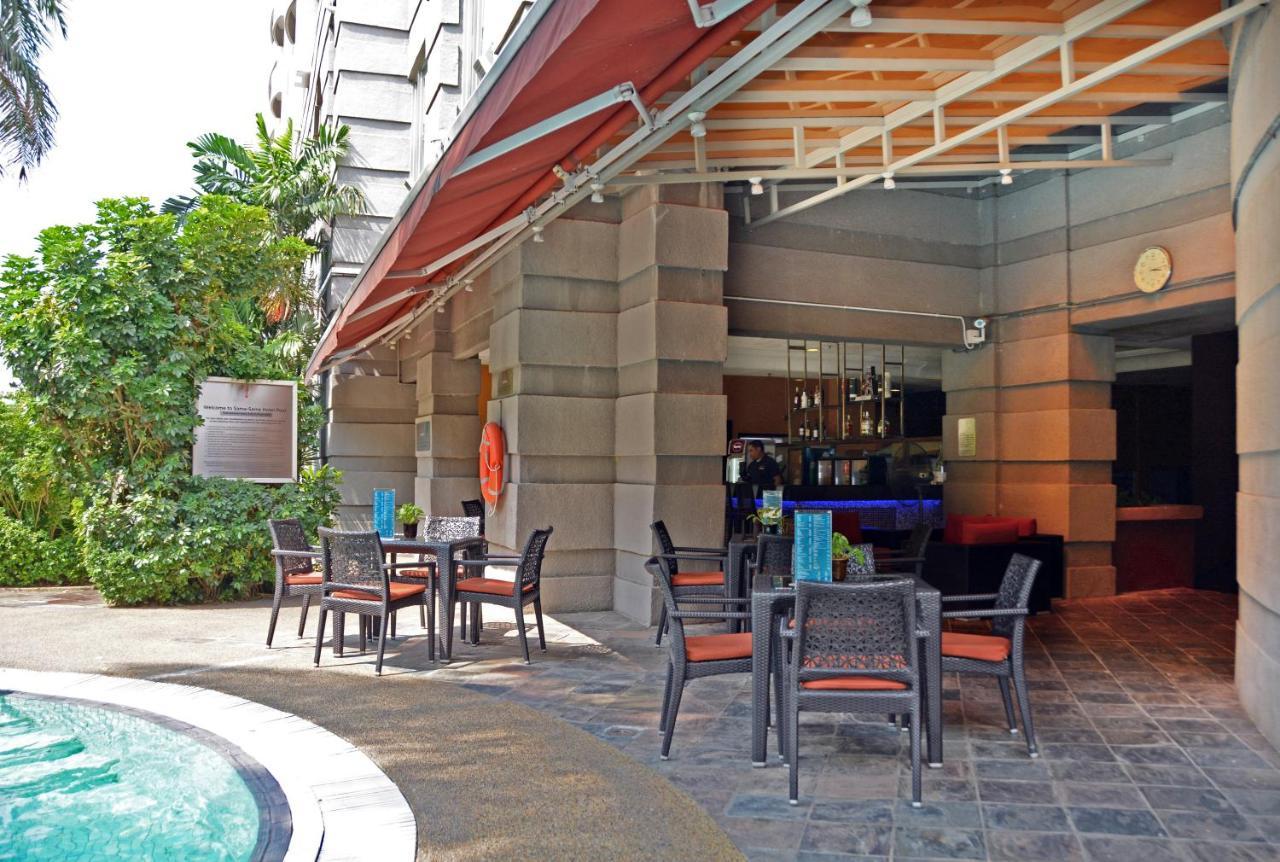 萨马萨玛克利亚酒店 雪邦 外观 照片 The photo shows an outdoor seating area next to a pool at a hotel or restaurant. There are several black wicker chairs with orange cushions arranged around small tables. The space is partially shaded by a large awning. In the background, there is a b