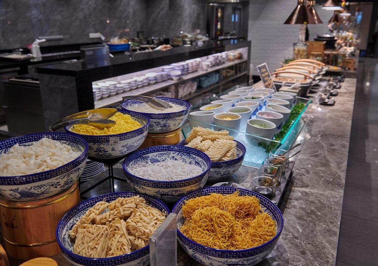 萨马萨玛克利亚酒店 雪邦 外观 照片 The photo shows a buffet setup featuring a variety of ingredients in large bowls and containers. There are different types of noodles, including yellow noodles and white rice, arranged in decorative bowls. Behind the bowls, a counter is visible with 